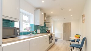 A modern kitchen with a microwave, sink, and cabinets. There is a dining area with a table and chairs. - Mews Retreat (Camborne)