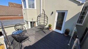 Una terrazza sul tetto con un pavimento in legno, due sedie in filo nero, un tavolino e piante in vaso.