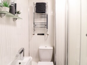 A bathroom with a glass shower enclosure, a white toilet, and a towel rack with a caution sign.