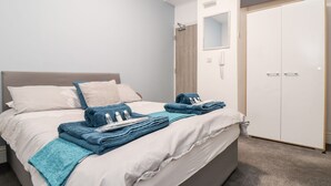 Un lit bien fait, agrémenté de serviettes et d’articles de toilette, une armoire blanche et une porte avec un miroir.