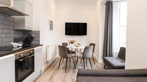 A modern kitchen with a built-in oven, a dining area with a table and chairs, and a seating area with a sofa. - Baker Chambers (Camborne)