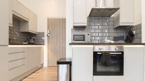 A modern kitchen with grey cabinets, a stainless steel range hood, a microwave, and an oven. - Baker Chambers (Camborne)