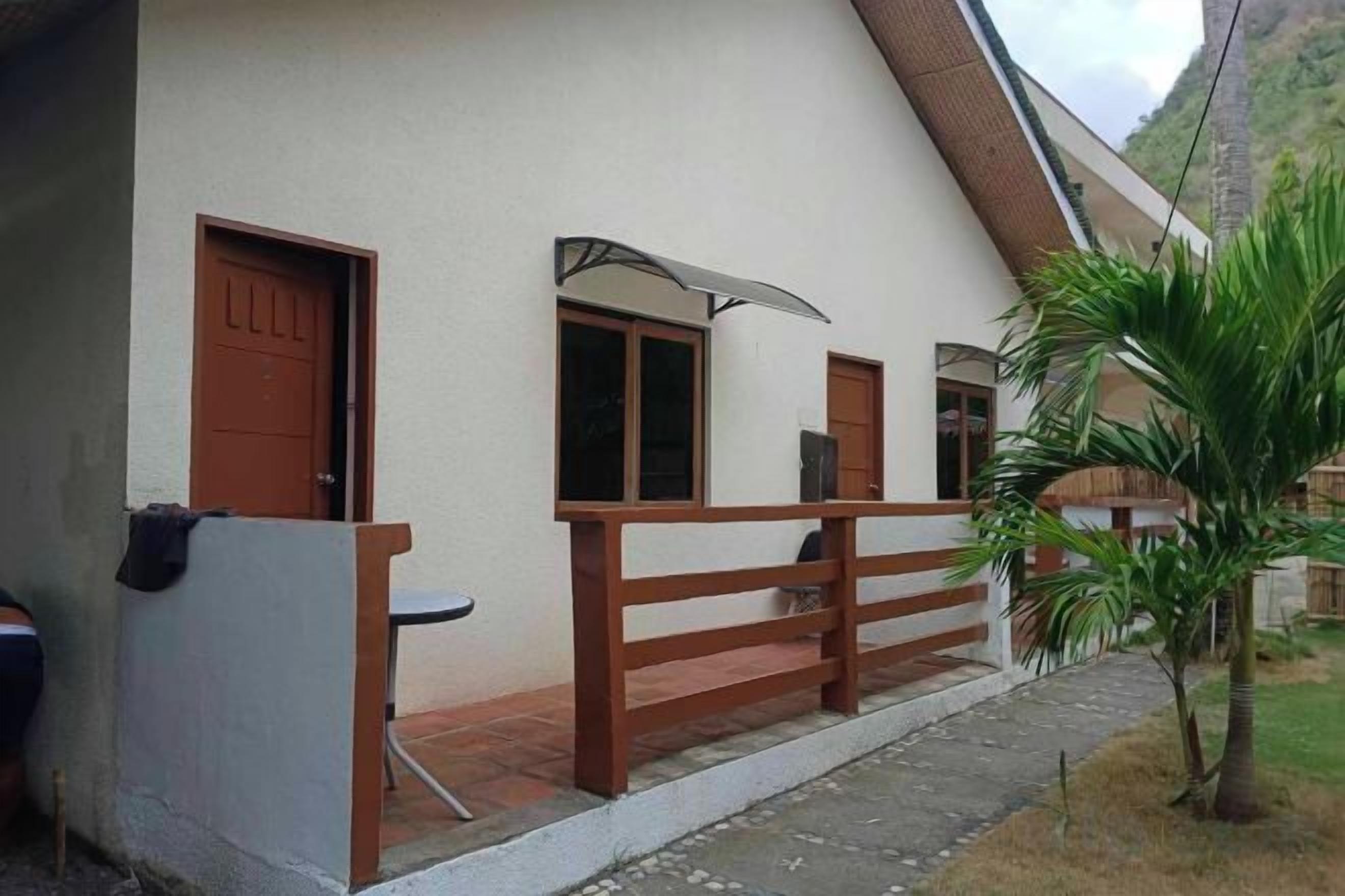 A single-story building with a sloped roof, a wooden fence, and a small garden area with a palm tree.