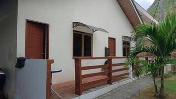 A single-story building with a sloped roof, a wooden fence, and a small garden area with a palm tree.