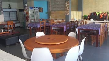 A dining area with round tables and chairs, a kitchen in the background, and a blue wall.