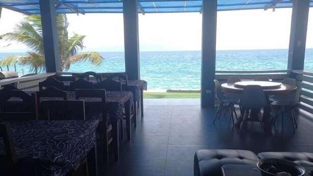 A covered outdoor seating area with tables and chairs, a sofa, and a view of the ocean. - Dolphin Bay Resort Puerto Galera (Abra de Ilog)