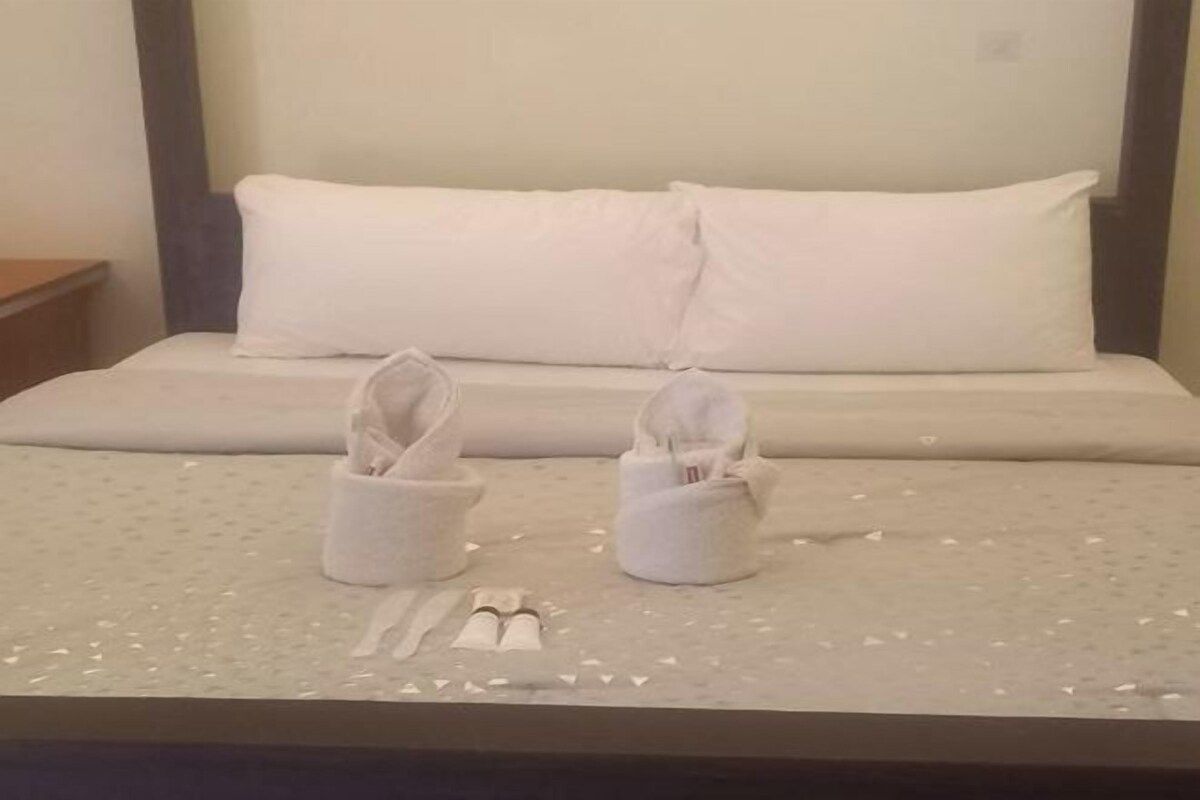 A neatly made bed with two white pillows and two white slippers placed on the bed.