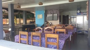 Un restaurante con sillas y mesas de madera, una zona de bar y un refrigerador.