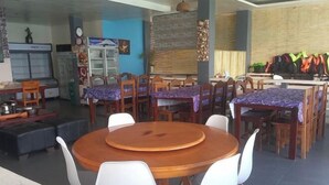 A dining area with round wooden tables and white chairs, a refrigerator, and a wall with a clock and a framed picture. - Dolphin Bay Resort Puerto Galera (Abra de Ilog)