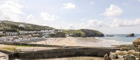 A coastal beach with a rocky foreground, a sandy beach, and a town with houses in the background.
