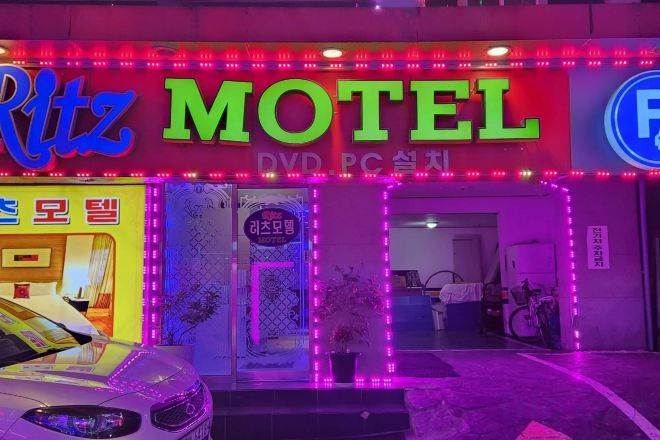A motel with neon signage, a visible entrance, and a parked car in front.