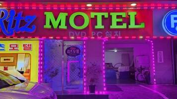 A motel with neon signage, a visible entrance, and a parked car in front.