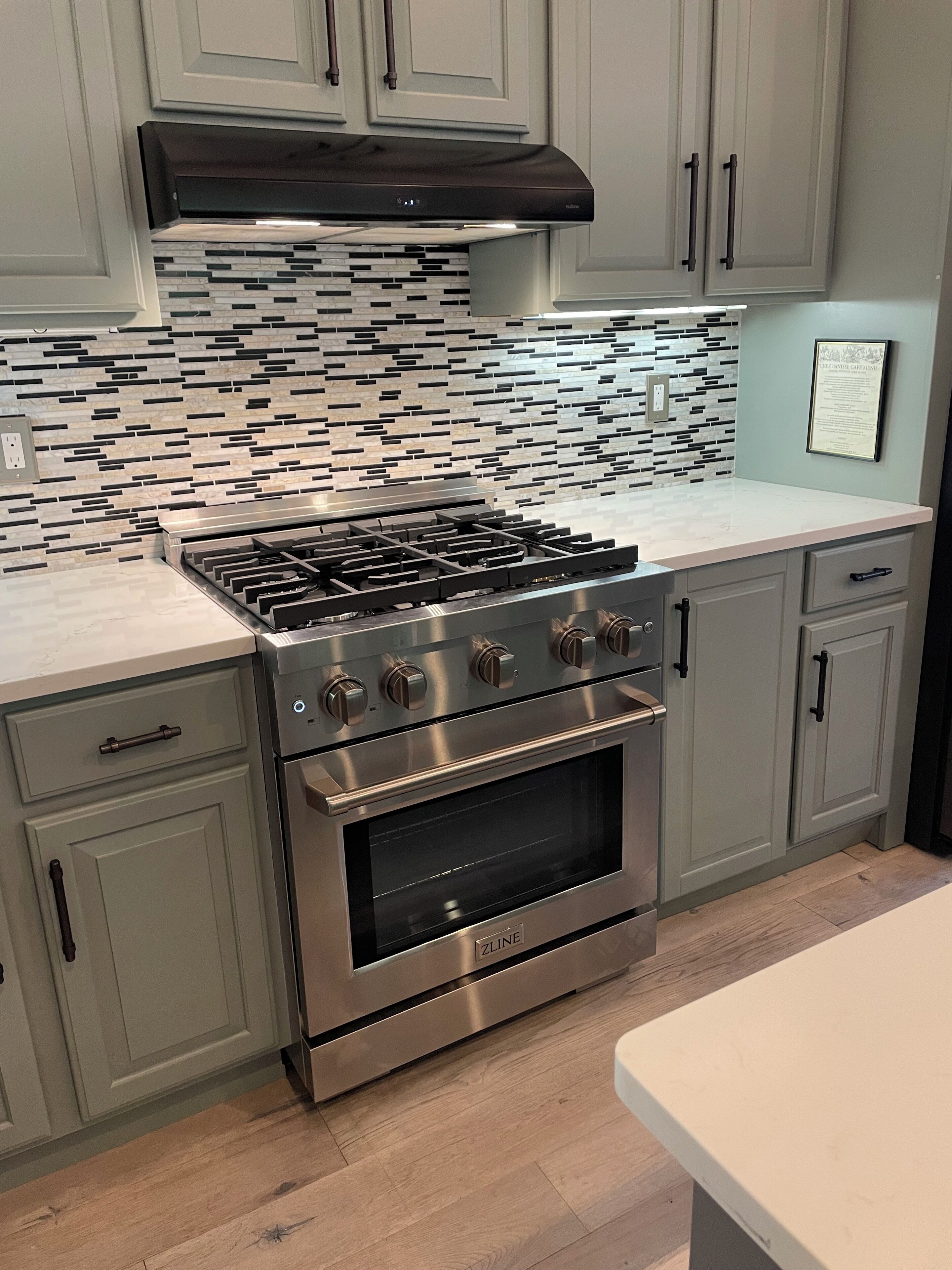 A modern kitchen with a gas stove, oven, and a backsplash with a mosaic tile design.