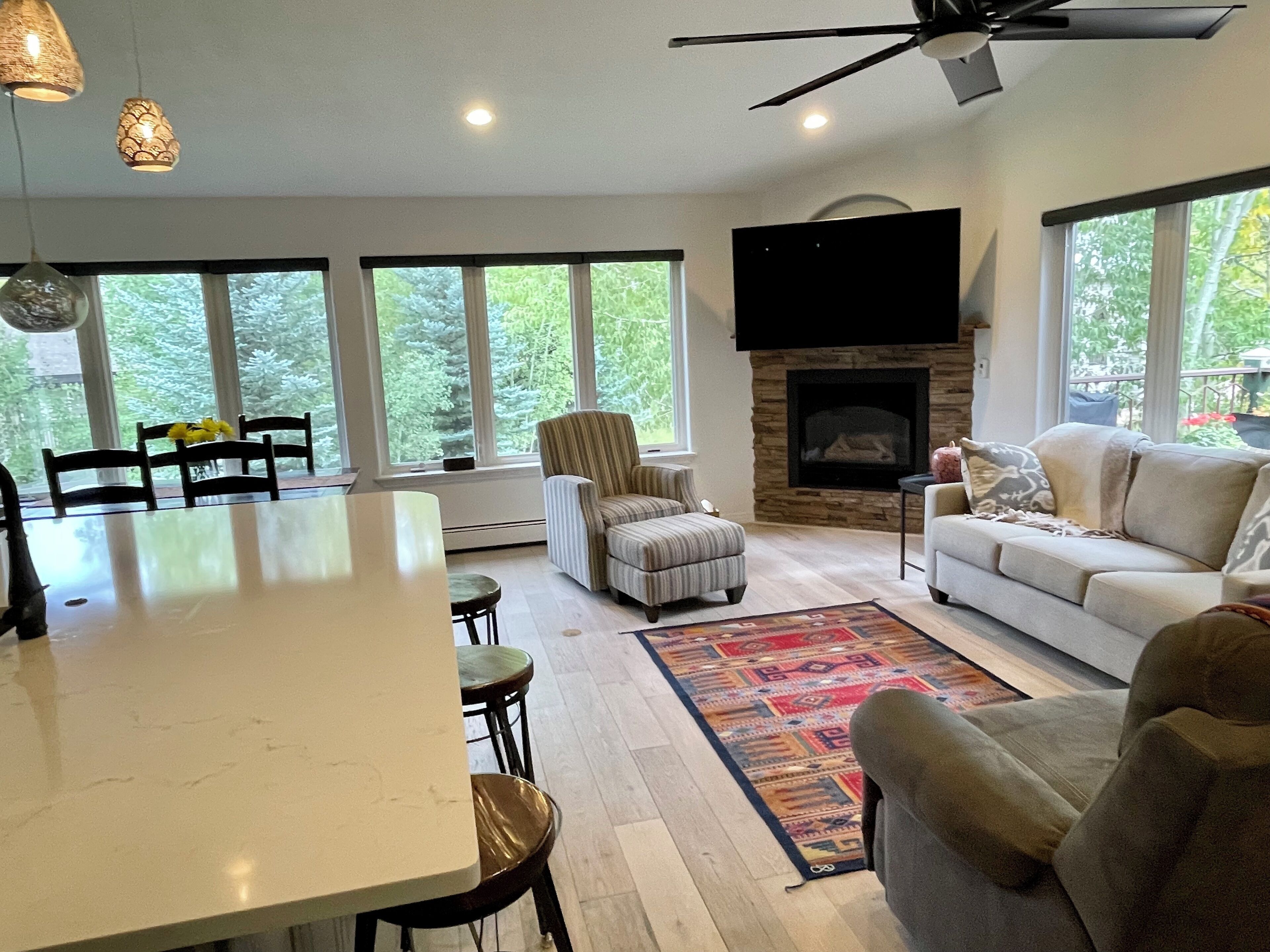 A spacious living area with a fireplace, large windows, and a ceiling fan.