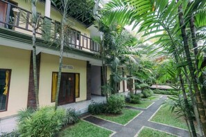 Un hotel de dos pisos, con un espacio exterior cubierto y plantas, y un sendero que lleva a la entrada.