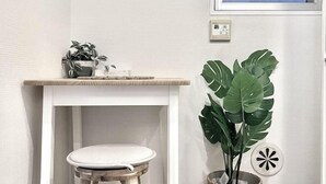 Une salle de bain avec un meuble-lavabo blanc, un tabouret blanc, une plante en pot et une fenêtre donnant sur un beau paysage.