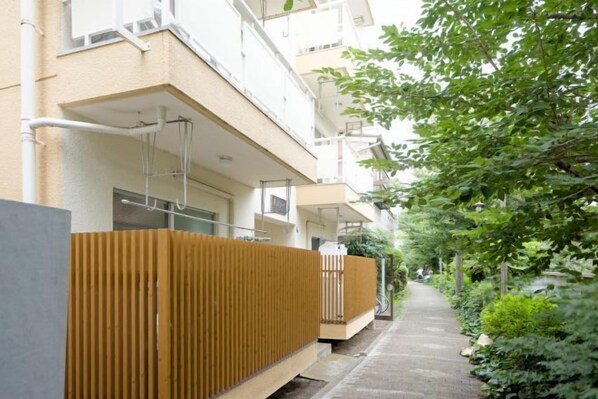 A narrow pathway flanked by apartment buildings with balconies, a wooden fence, and greenery. - Shinjuku Waseda Fujitaki Apartment (Tokyo)