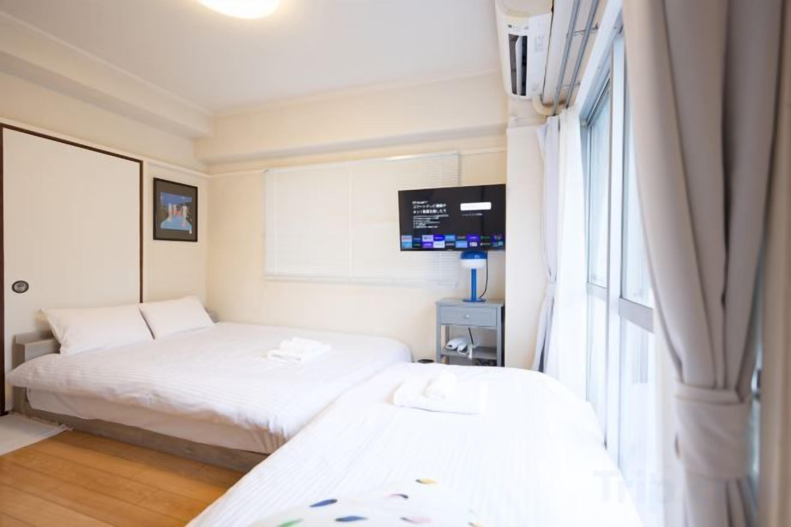A hotel room with two beds, a television, and a window with curtains.