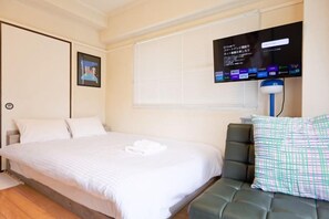 Une chambre d’hôtel avec un lit, un téléviseur fixé au mur et une fenêtre avec des stores.