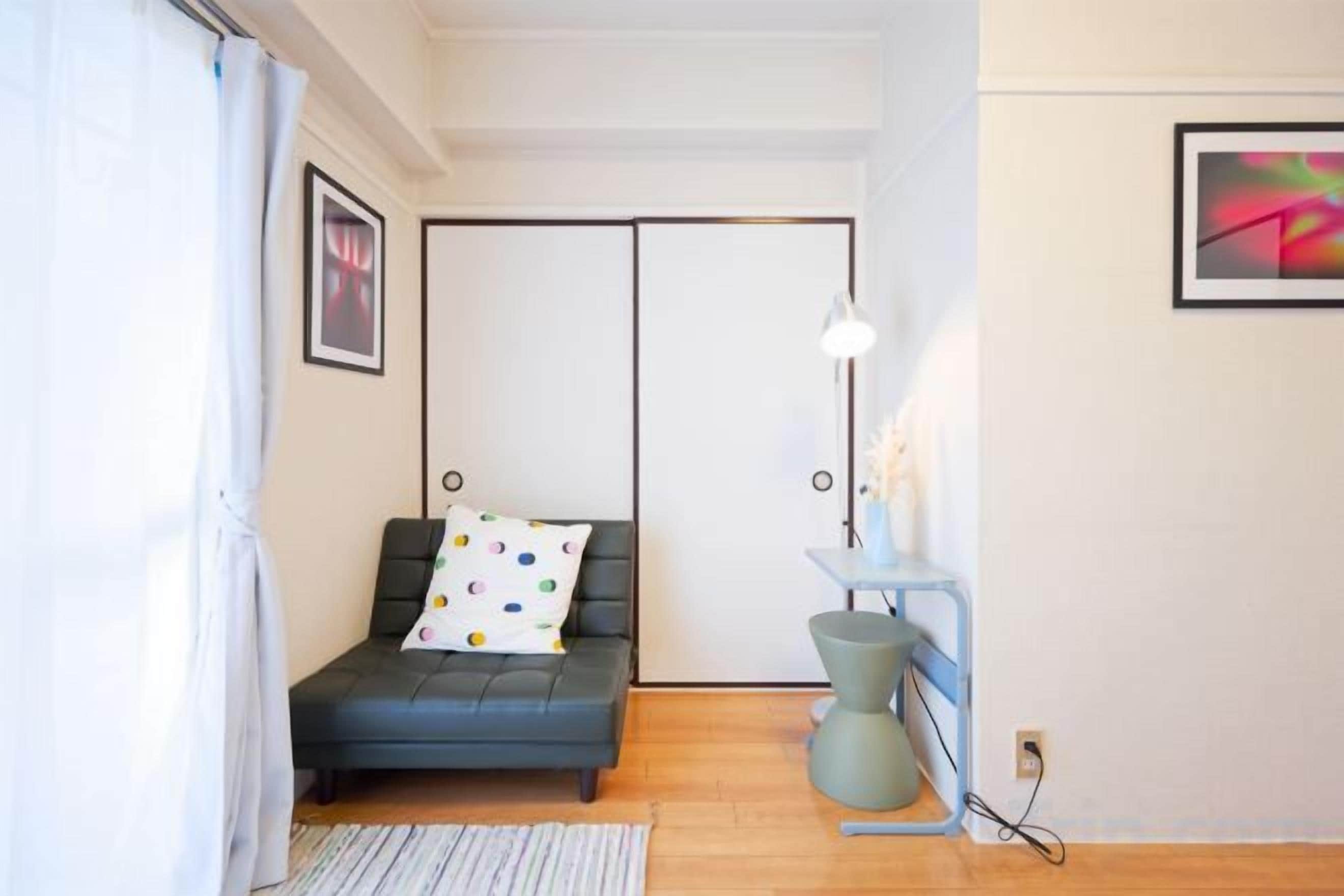 A room with a sofa, a small table with a lamp, a picture on the wall, and a window with curtains.