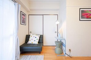 Une pièce avec un canapé, une petite table avec une lampe, un tableau au mur et une fenêtre avec des rideaux.