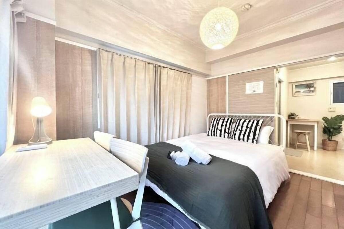 Une chambre d’hôtel avec un lit, un bureau, une chaise, une lampe, une plante en pot et une petite table.