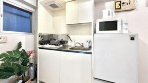 Une cuisine de taille réduite, dotée de meubles blancs, d’un four à micro-ondes, d’un réfrigérateur, d’un évier et d’une cuisinière.
