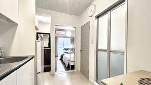 Un couloir étroit, avec un coin cuisine d’un côté et une chambre à coucher visible à travers une porte ouverte.