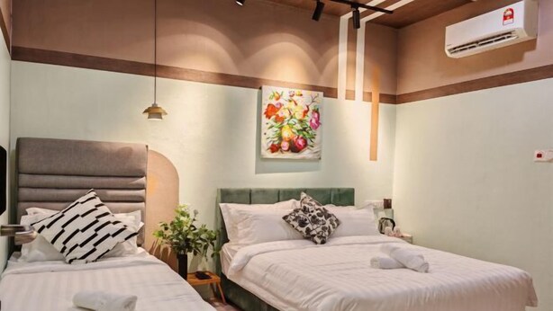 Quarto de hotel com duas camas, cabeceira verde, pintura floral e luminária no teto.