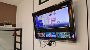 Televisão de tela plana na parede exibindo um vídeo do YouTube com uma mulher e texto.