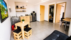 Een ruimtelijk ingedeelde leefruimte met kitchenette, een eethoek met een houten tafel en bankjes, en een aparte tafel met stoelen.