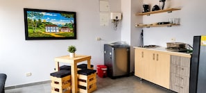 A compact kitchen with a refrigerator, a sink, and wooden cabinets. There is a small table with a potted plant and a red trash bin.