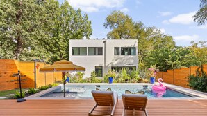 Uma casa moderna com piscina, deck de madeira e cadeiras de descanso.