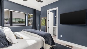 Quarto moderno com uma cama grande, ventoinha no teto, televisão na parede e janela com cortinas.