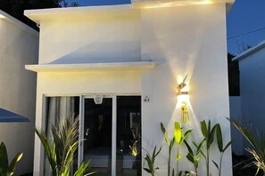 Un edificio moderno con fachada blanca, una entrada visible con puertas de vidrio y un pequeño espacio exterior con plantas.