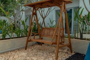 Un ensemble de balançoires en bois installé dans un jardin, avec des graviers au sol et différentes plantes en arrière-plan.