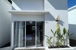 Un edificio moderno con puerta de entrada de vidrio corredera, un pequeño espacio exterior con plantas y cielo despejado.