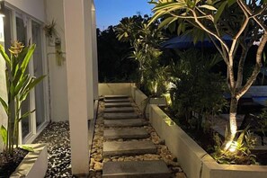 Una escalera de piedra lleva a la entrada de un edificio, rodeada de plantas en macetas y un pequeño jardín.