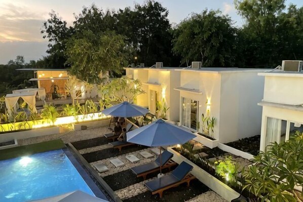 A modern outdoor pool area with lounge chairs and umbrellas, surrounded by greenery and white buildings. - Bella Belly Cottage by Bali Cabin (Bali)