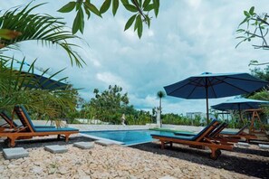 Un área de piscina con sillones de descanso y sombrillas, rodeada de vegetación.