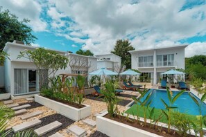 Un espace moderne aménagé au bord de la piscine, avec des chaises longues, une piscine et un immeuble à plusieurs étages doté de balcons.
