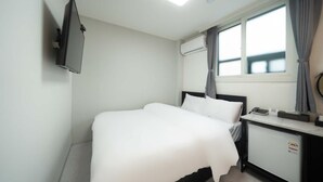 A hotel room with a bed, a desk with a telephone, an air conditioning unit, and a window with curtains. - Doksan White (Seoul)