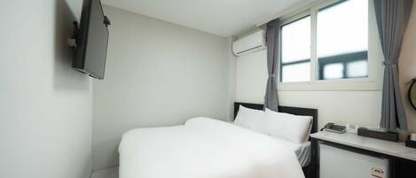 Une chambre d’hôtel équipée d’un lit, d’un bureau avec un téléphone, d’un appareil de climatisation et d’une fenêtre avec des rideaux.