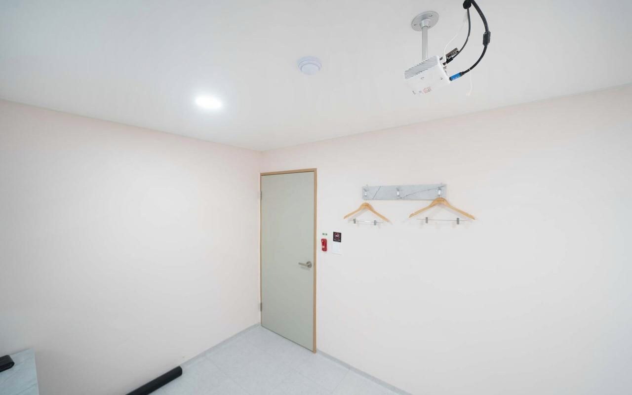 A room with a door, a ceiling-mounted light fixture, and a wall-mounted shelf with a hanging item.