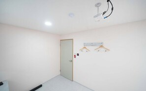 A room with a door, a ceiling-mounted light fixture, and a wall-mounted shelf with a hanging item. - Doksan White (Seoul)