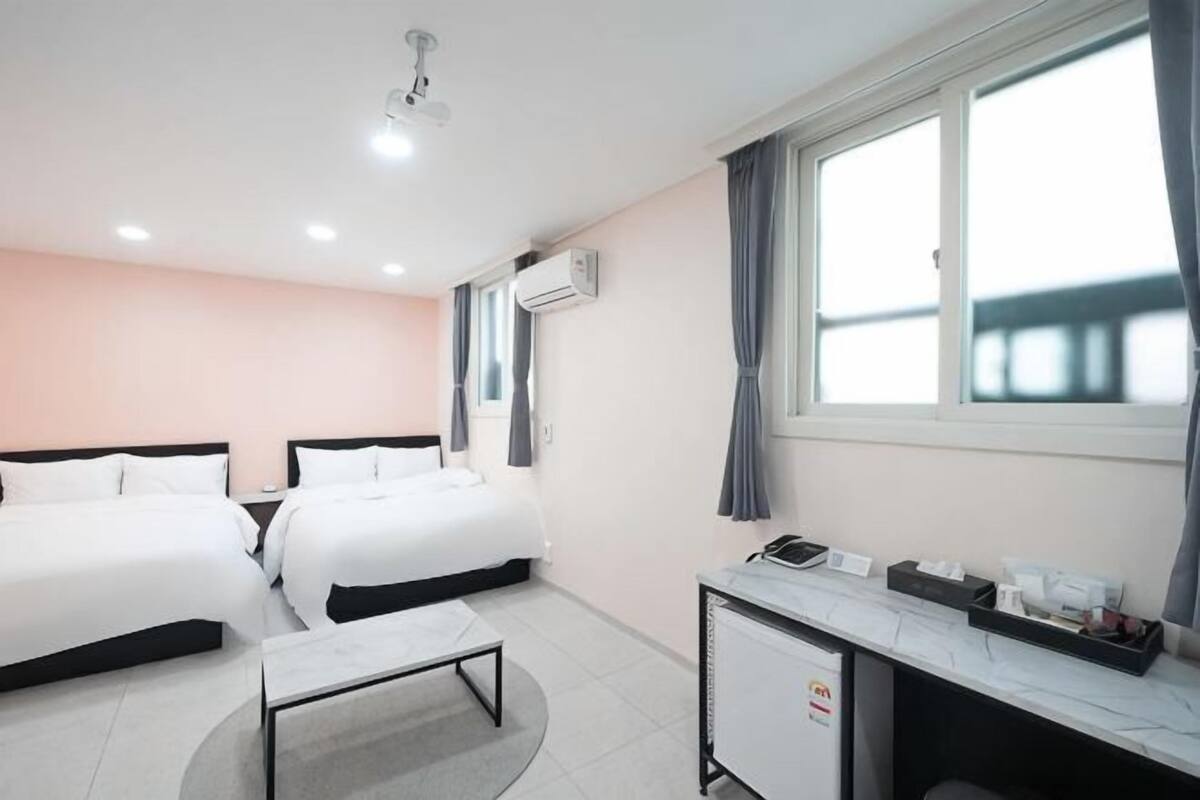 A hotel room with two beds, a desk, a chair, a small table, and a window with curtains.