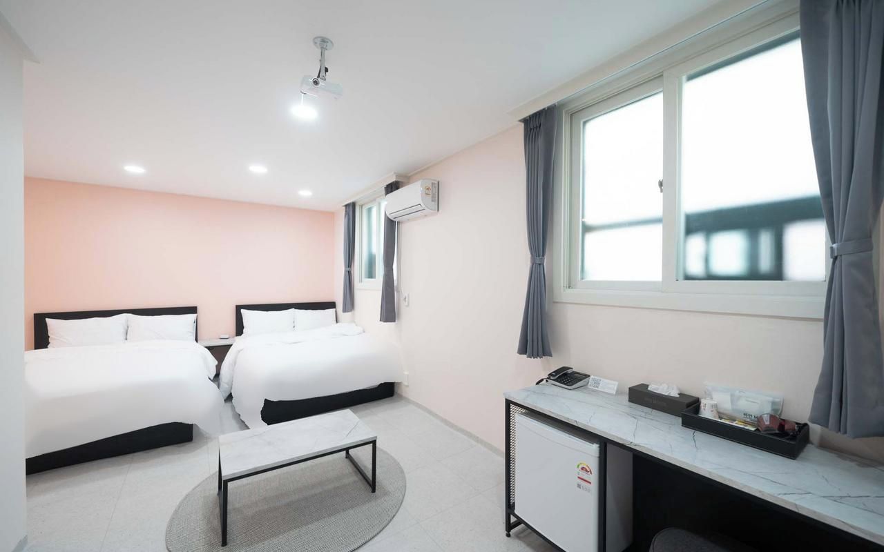 A hotel room with two beds, a desk, a small table, and a window with curtains.