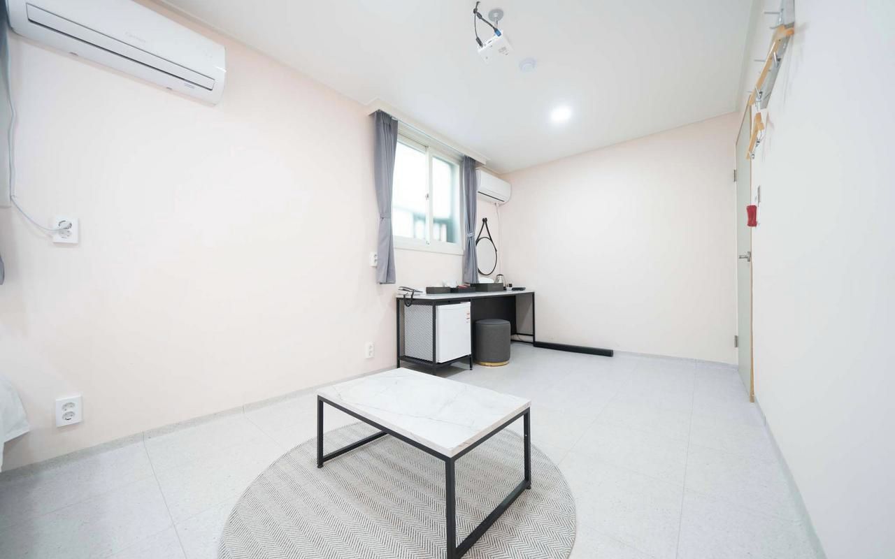 Une pièce avec un climatiseur blanc, une petite table à structure métallique, une fenêtre avec des rideaux et un bureau avec une chaise.
