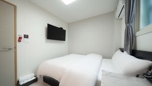 A hotel room with a bed, a flat-screen TV mounted on the wall, a window with curtains, and a small bedside table. - Doksan White (Seoul)