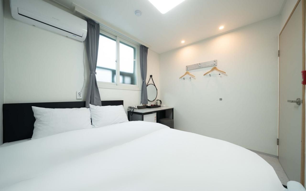 Une chambre d’hôtel avec un grand lit, un bureau avec une chaise, un porte-manteau et une fenêtre avec des rideaux.
